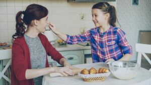 Young girl helping her mother at home, smiling while preparing food together.